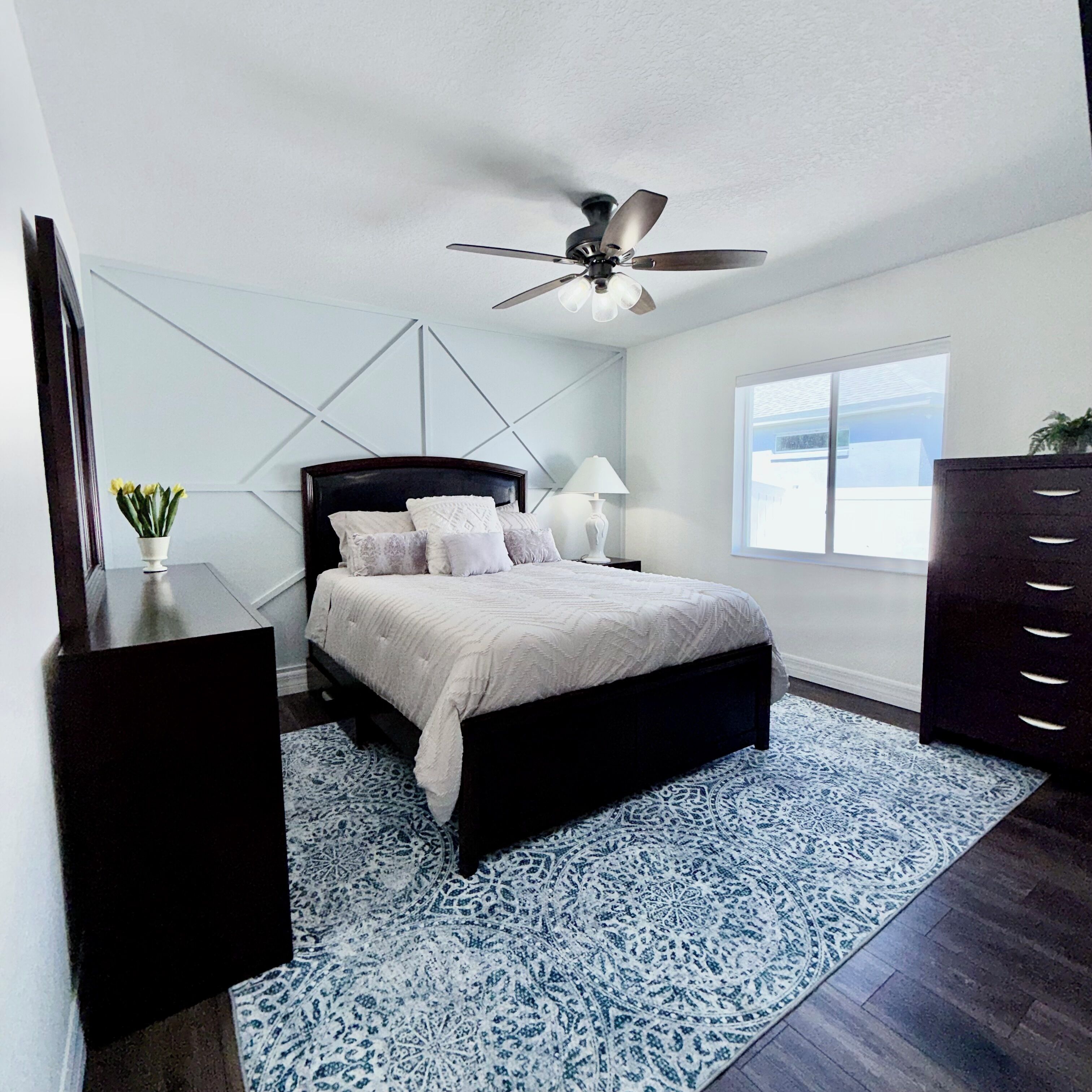 A bedroom with a bed, a ceiling fan, a window, and a dresser.