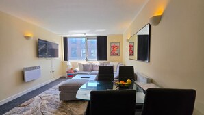 Un salon moderne avec un canapé, une table basse en verre et un téléviseur fixé au mur.