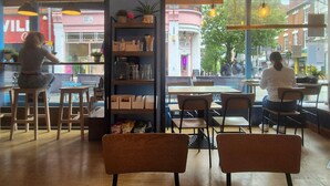 Un espace de repos intérieur avec des tables et des chaises, un comptoir et une grande fenêtre donnant sur la rue.