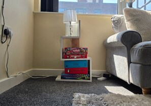 A corner of a room with a lamp, a stack of board games, and a grey sofa. - Stylish 1BR Flat Next to Hockley (Nottingham)