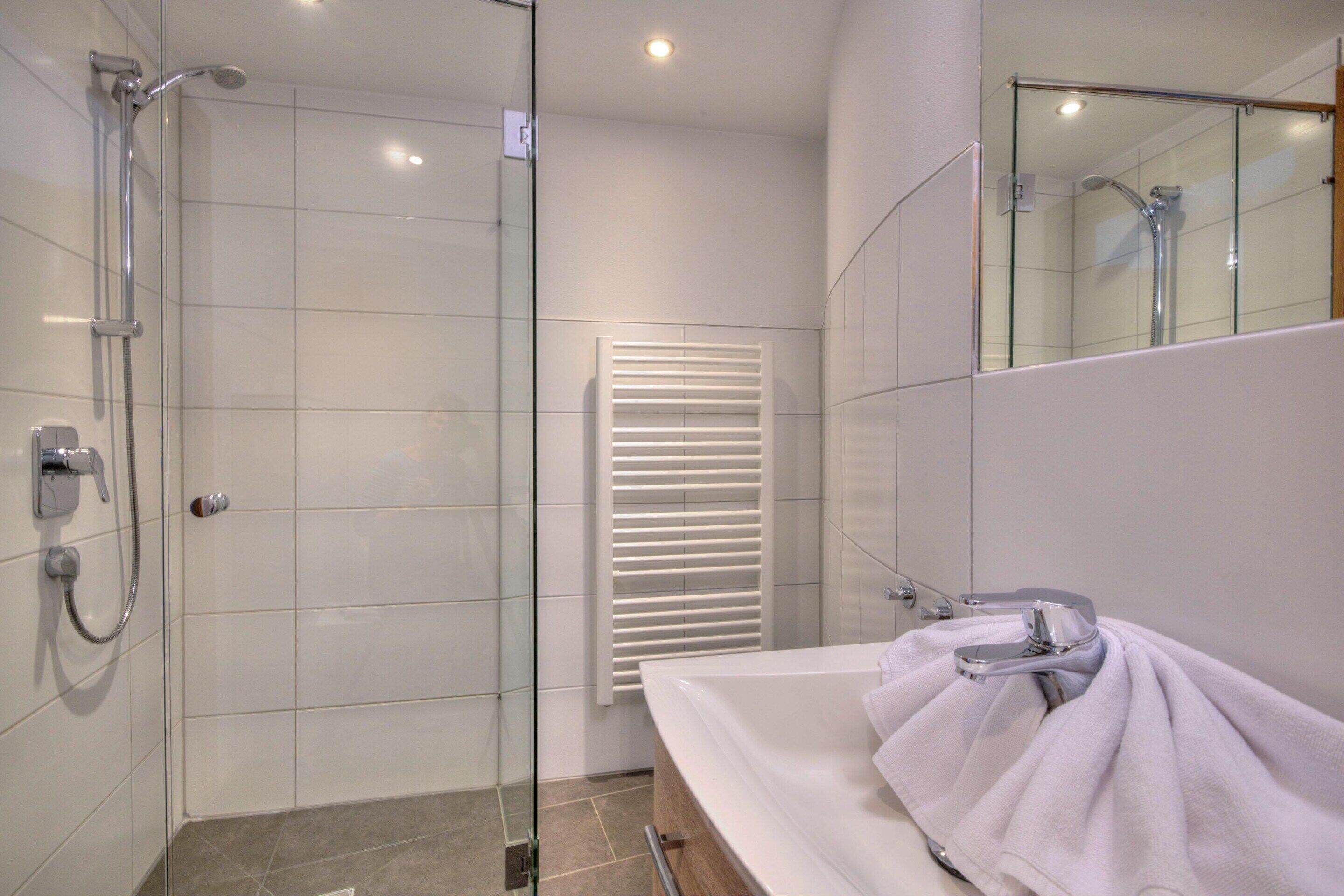 A modern bathroom with a glass-enclosed shower, a white sink, and a towel on the counter.