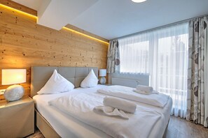 A hotel room with a wooden headboard, a large bed with white linens, a bedside table with a lamp, and sheer curtains on the window. - Brunner Apartment on the ski Slope (Wildschönau)