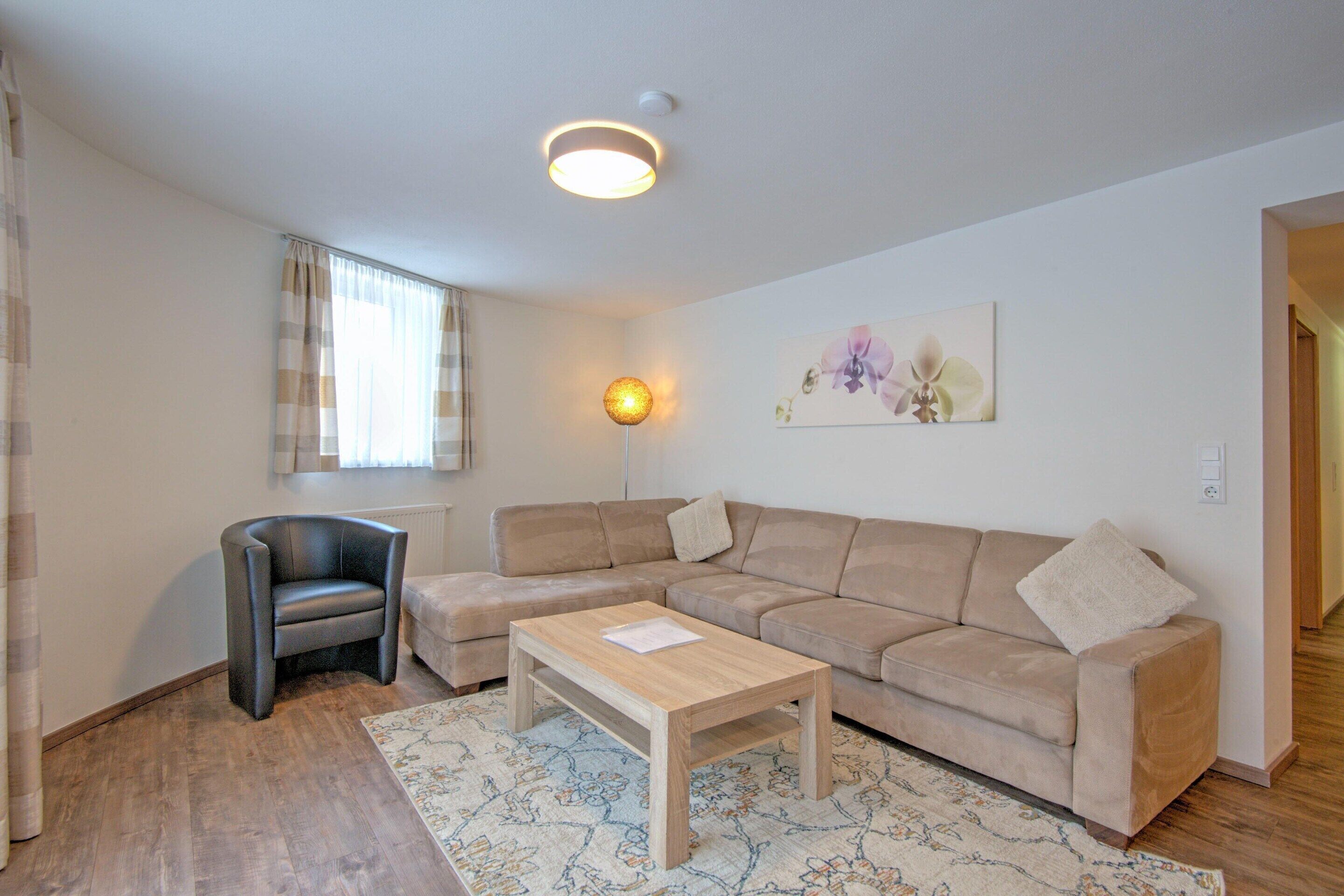 Un salon avec un canapé, un fauteuil, une table basse, une lampe et un tableau accroché au mur.