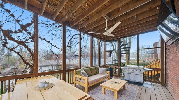 A covered outdoor deck with a wooden table, a sofa, and a grill. - Historic Tower Grove Retreat (St. Louis)