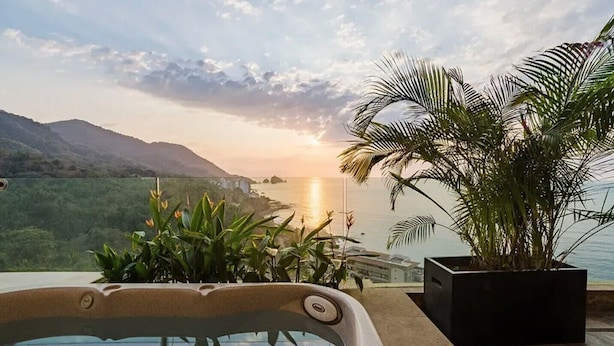 Un jacuzzi con vistas al océano y montañas al atardecer.