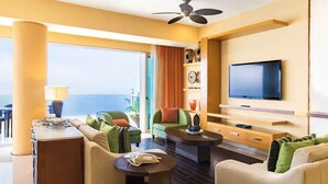 Una sala de estar moderna con un sofá, sillones, una mesa de centro y una televisión. Cuenta con un balcón con vistas al océano.