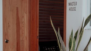Une porte en bois avec une poignée en métal, un pot de fleurs et une pancarte sur le mur indiquant « MAISON PRINCIPALE ».