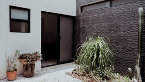 Un bâtiment moderne avec une façade à l’aspect pierre, une entrée avec une porte-fenêtre coulissante et des plantes en pot.