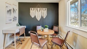 A dining area with a round wooden table, four brown leather chairs, a macrame wall hanging, and a window with a view of trees.