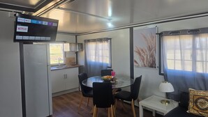 A compact living space with a kitchenette, dining area, and a TV mounted on the wall displaying Netflix.