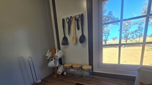 A kitchen with wooden cabinets, a black stove, hanging kitchen utensils, and a window with a view of a field.