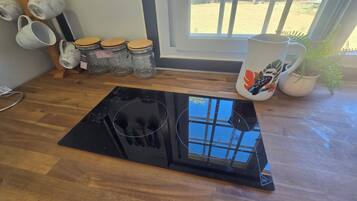 Una cocina con tope de inducción negro, armarios de madera y una ventana que da a un área exterior cercada.