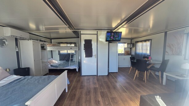 A compact RV interior with a bunk bed, kitchenette, dining area, and a TV mounted on the wall.