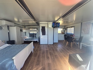 A compact RV interior with a bunk bed, kitchenette, dining area, and a TV mounted on the wall.