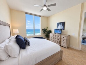 Un dormitorio con una cama grande, ventilador de techo, cómoda y vista al océano.