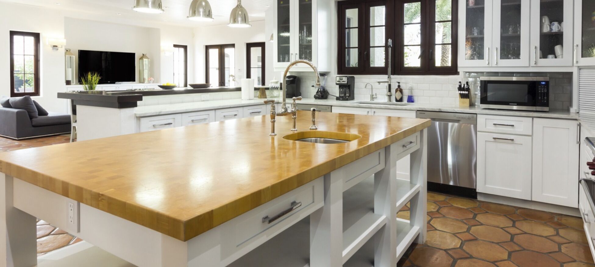 Una cocina moderna con armarios blancos, una isla de madera con un lavamanos, electrodomésticos de acero inoxidable y un amplio ventanal que proporciona luz natural.