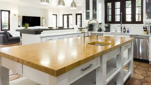 A modern kitchen with white cabinetry, a wooden island with a sink, stainless steel appliances, and a large window providing natural light. - World Cup 2026 Dream Villa 3 (Miami)