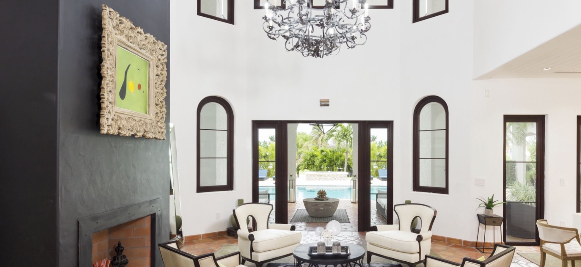 A spacious living room with a fireplace, a chandelier, and a view of a pool.