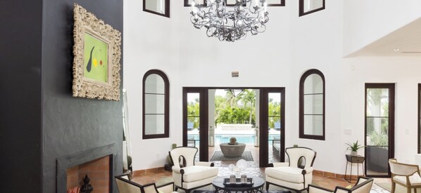A spacious living room with a fireplace, a chandelier, and a view of a pool.