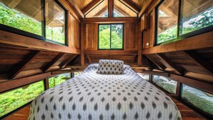 Eine Holzhütte mit Bett, großen Fenstern und Blick auf Grün.
