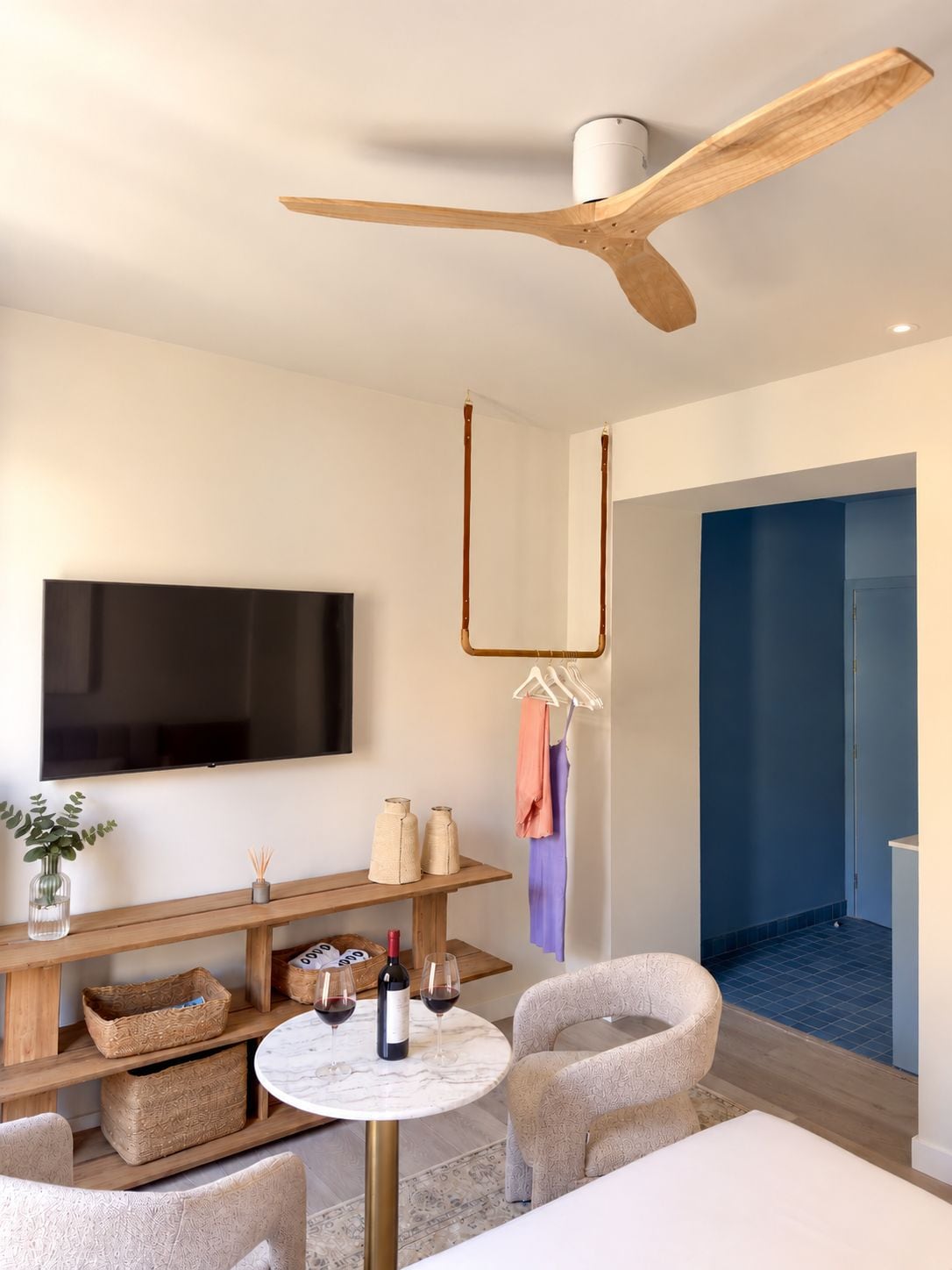 Una sala de estar moderna con un televisor de pantalla plana, muebles de madera, una mesa redonda con copas de vino y un ventilador de techo.