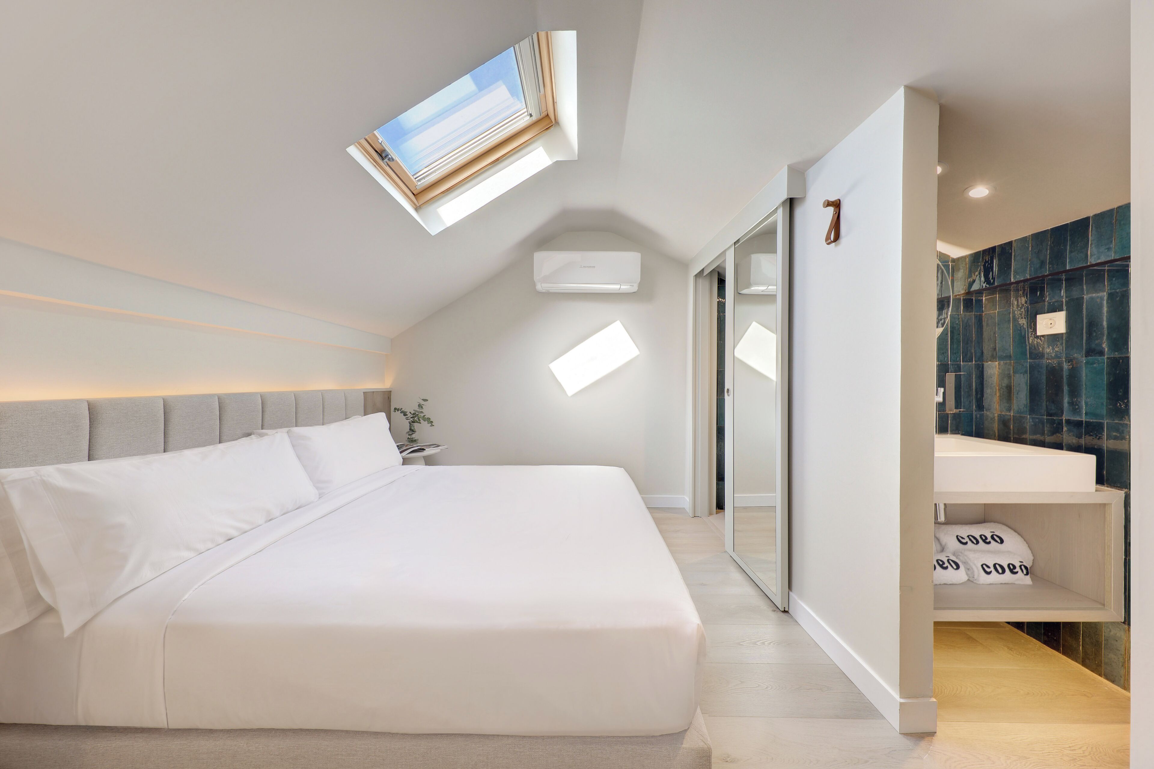 Een moderne slaapkamer met dakraam, een bed met witte beddengoed, een nachtkastje en een ingebouwde plank met kussens.