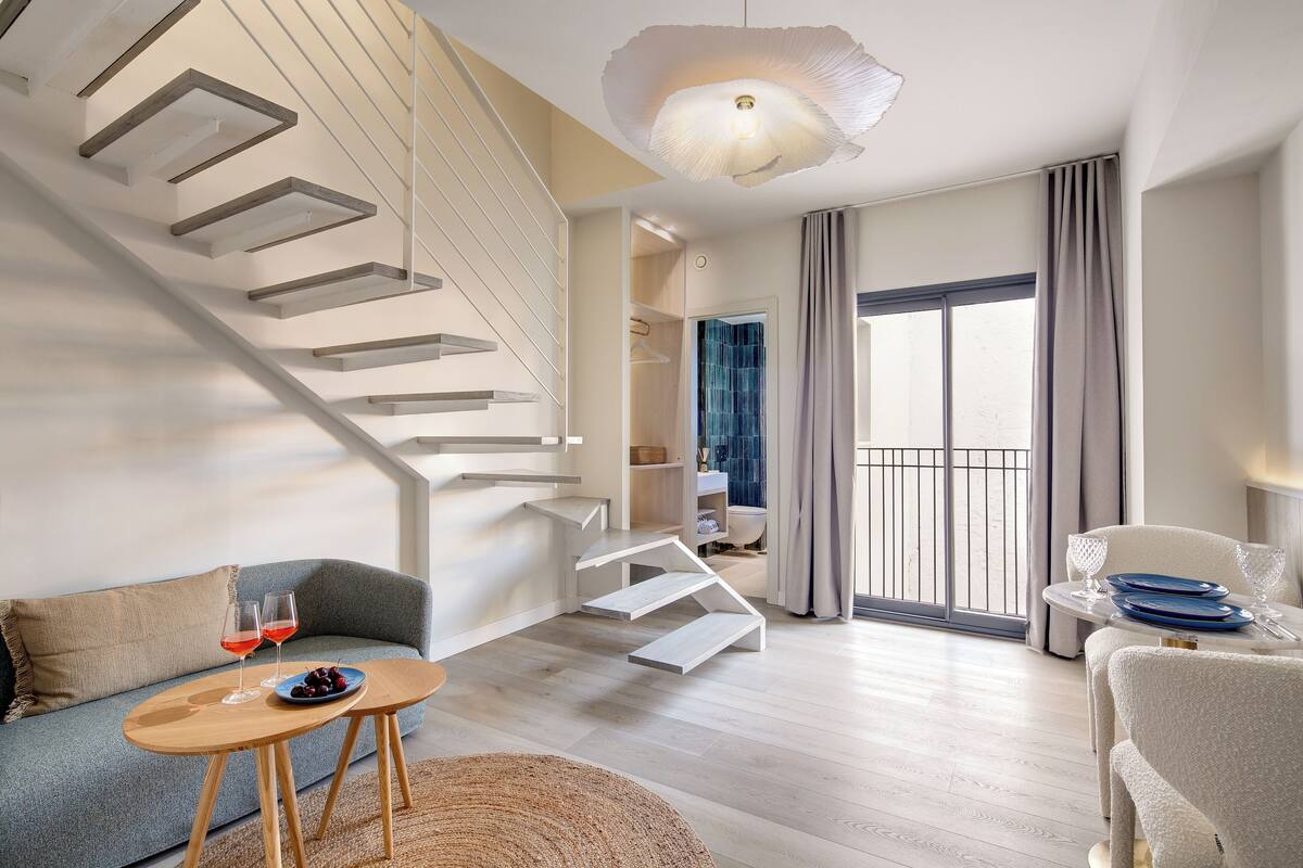 Ein modernes Wohnzimmer mit Treppe, Sofa, Esstisch und Blick ins Freie.