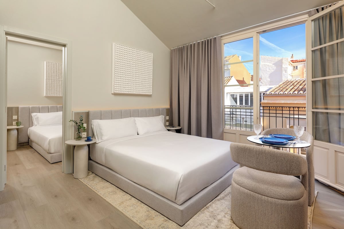Ein modernes Hotelzimmer mit einem großen Bett, einem kleinen Tisch mit einem Stuhl und Blick auf die Stadt durch große Fenster.