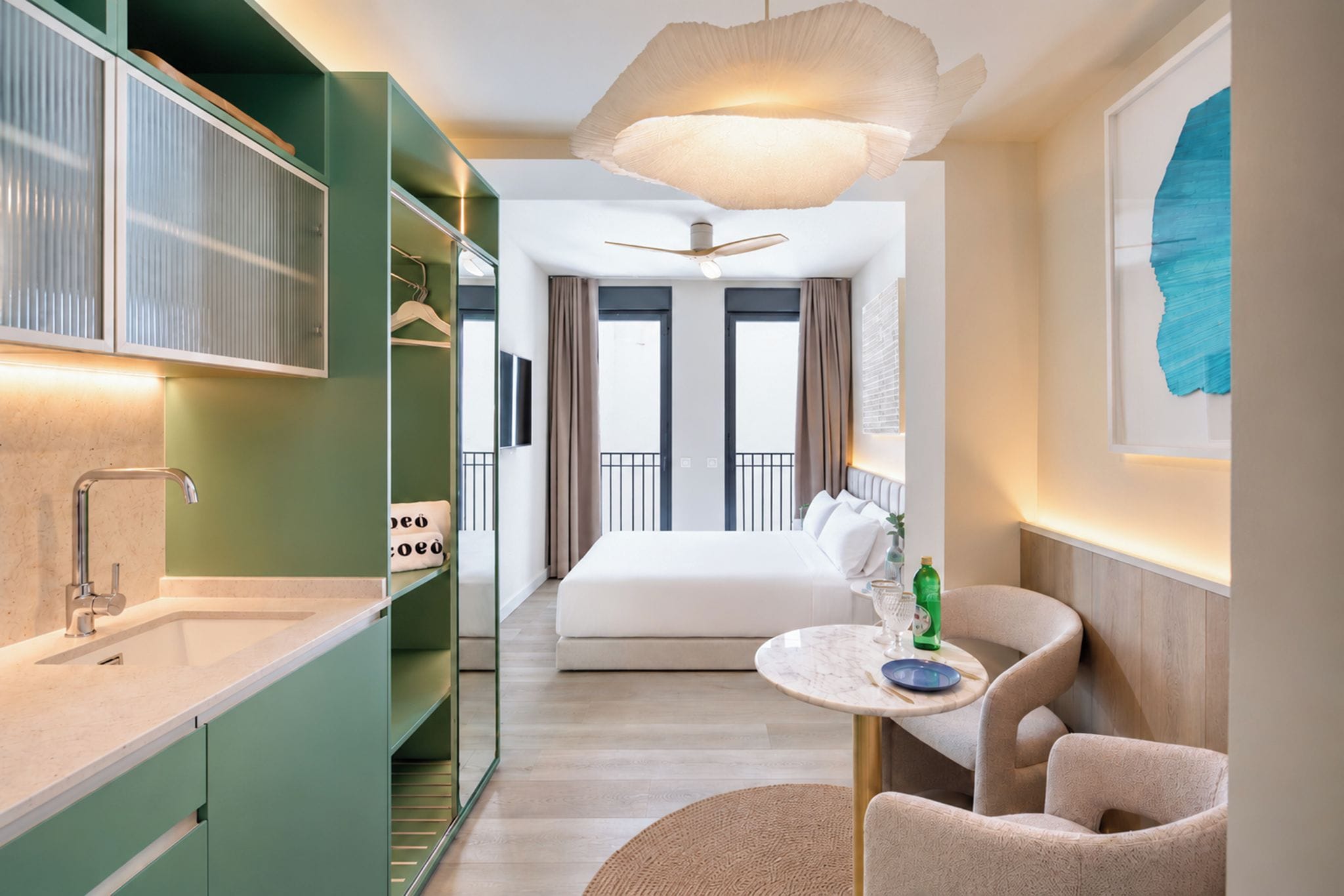 Ein modernes Hotelzimmer mit Bett, kleinem Esstisch, Sitzecke, Badezimmer mit Spiegel und großem Fenster.