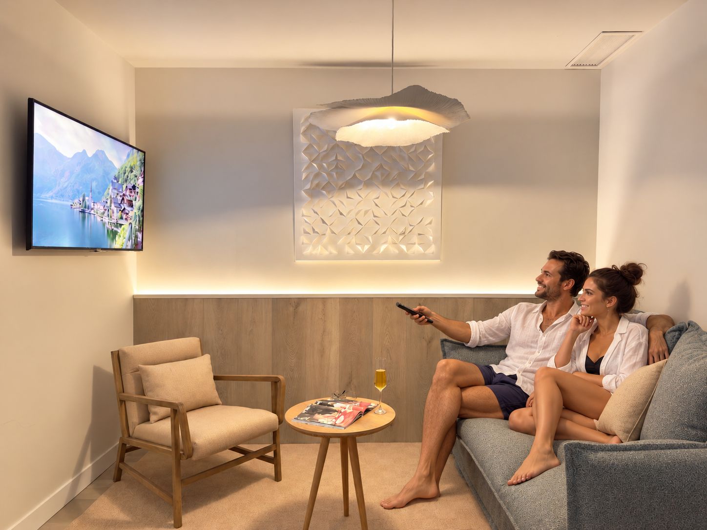 Een moderne woonkamer met een flatscreen televisie, een houten stoel, een klein rond tafeltje met een glas wijn, en een bank met twee personen erop.