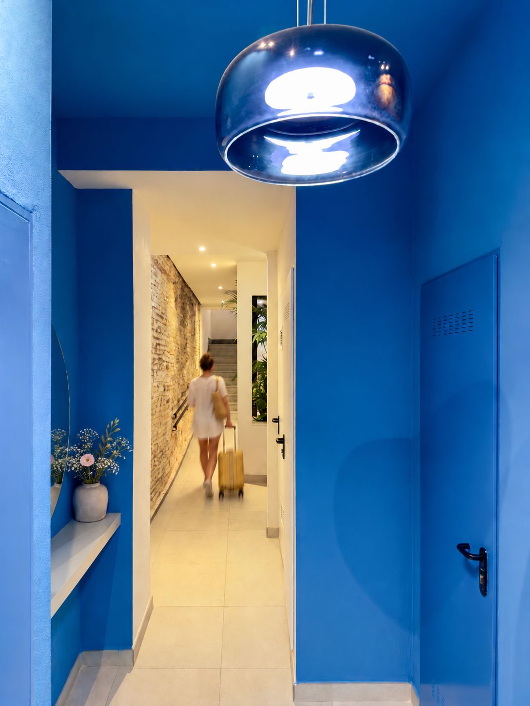 A hallway with a blue wall and a person walking with a suitcase.