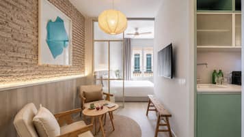 Habitación de hotel moderna con pared de ladrillo, un ventanal grande, televisor de pantalla plana, un banco de madera y una mesa redonda con un vaso.