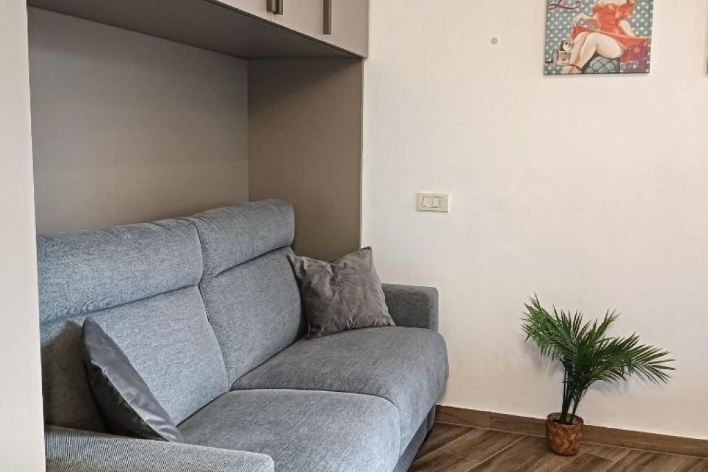 Un divano grigio con cuscini grigi, una piccola pianta in vaso e un interruttore della luce fissato al muro.