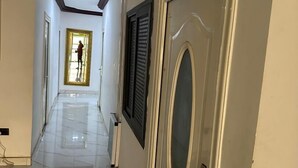 A hallway with a polished floor, a door with a decorative handle, and a person standing in the distance. - GQ Luxury Hills Hotel- Akropong Akwapim (Akropong)