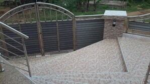 A gated entrance with a metal gate and a stone wall, leading to a tiled area with a metal railing. - GQ Luxury Hills Hotel- Akropong Akwapim (Akropong)