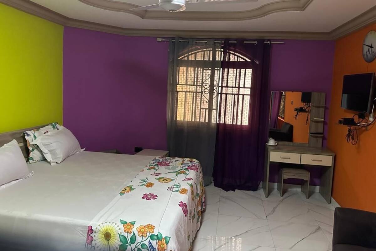 A bedroom with a bed, a desk, a chair, a ceiling fan, and a window with bars.
