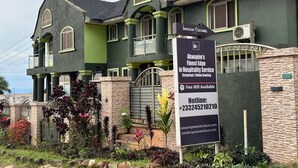 A two-story building with a green facade, a signboard advertising Akwapim's hospitality services, and a gated entrance. - GQ Luxury Hills Hotel- Akropong Akwapim (Akropong)