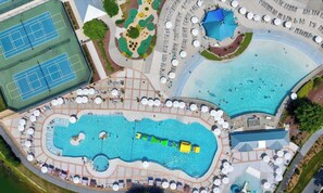 Luchtbeeld van een resort met meerdere zwembaden, een tennisbaan en ligbedden.