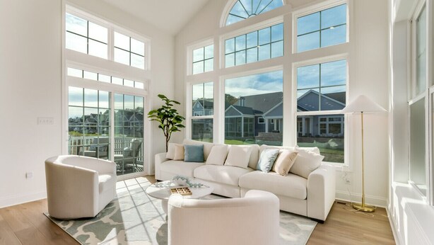A spacious living room with a white sofa, a round coffee table, and a large window offering a view of a residential area. - Resort Retreat: King Suites & Nature Trails (Millsboro)