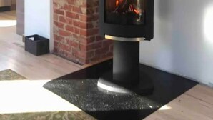 Una sala moderna con un estufa de leña negra, una chimenea de ladrillo y una escalera.