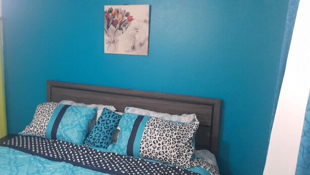 Una cama con una colcha estampada y varias almohadas, una pared azul y un cuadro enmarcado sobre la cama.
