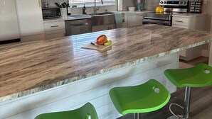 Une cuisine moderne avec des meubles blancs, un plan de travail en granit et des tabourets de bar verts.