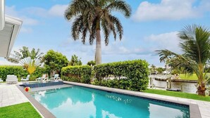 Une piscine à l’eau d’un bleu cristallin, entourée de haies verdoyantes et de palmiers.