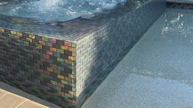 Un bassin rectangulaire orné d’une bordure en mosaïque, entouré d’une zone pavée et d’une végétation luxuriante.