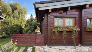 A wooden cabin with a number 29 sign, a window with curtains, and a small garden area with a wooden fence and steps leading to the entrance. - Madeira House (Starzach)