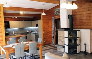 Interior acollidor d'una cabana amb zona de menjador, cuina i una estufa de llenya.