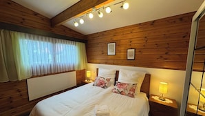 A neatly made bed with a white comforter and floral pillows, a bedside table with a lamp, and a window with sheer curtains. - Madeira House (Starzach)