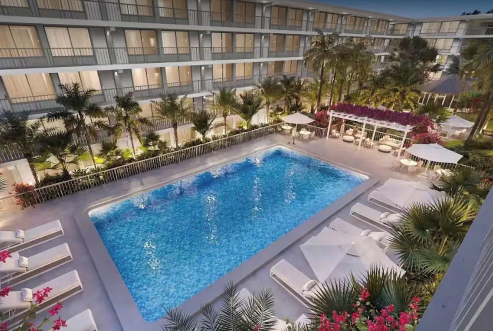 A rooftop pool with a view of a modern building, surrounded by palm trees and lounge chairs.