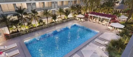 Une piscine sur le toit offrant une vue sur un bâtiment moderne, entourée de palmiers et de chaises longues.