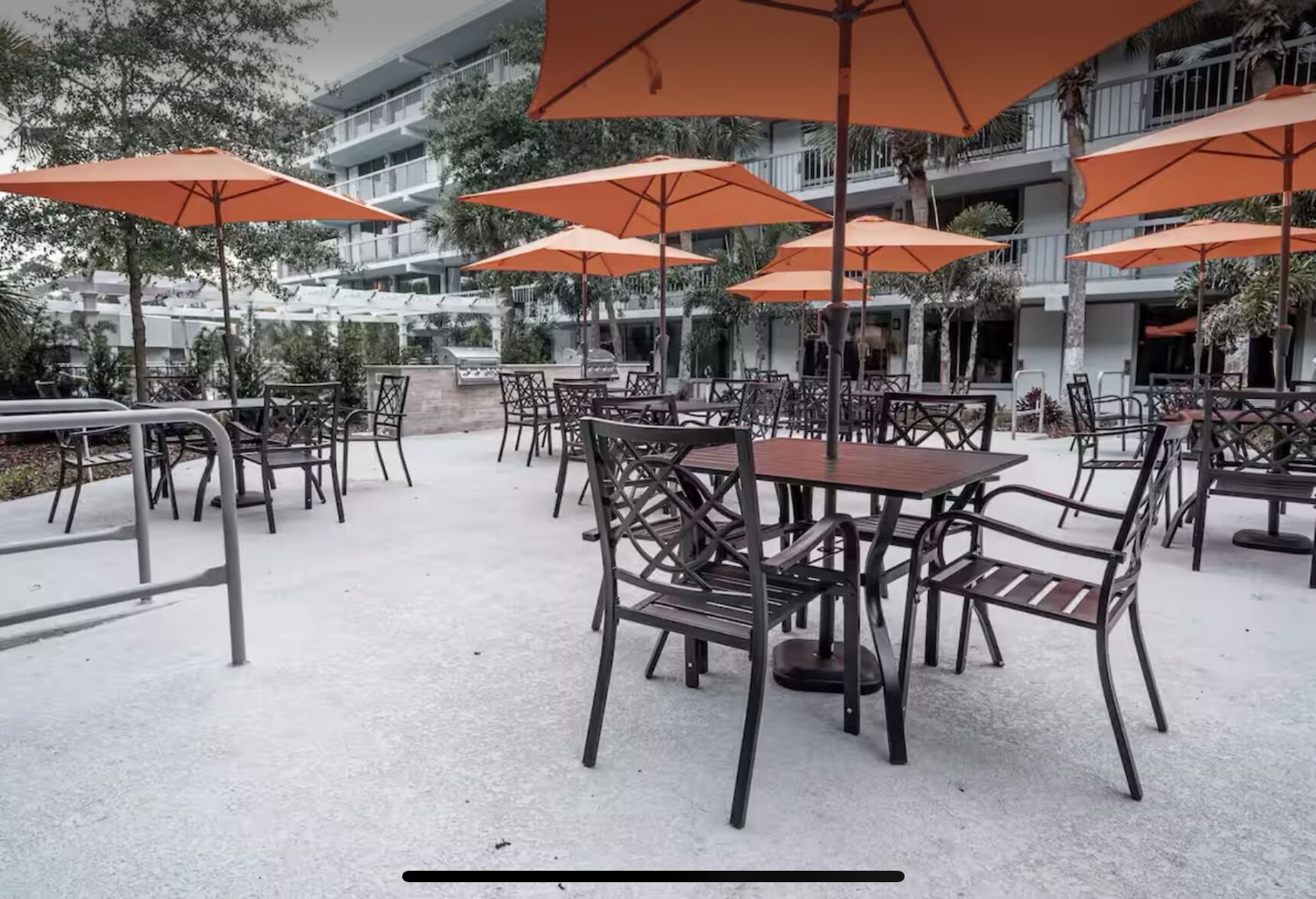 Outdoor seating with tables and chairs, surrounded by orange umbrellas, in a courtyard with a building in the background.